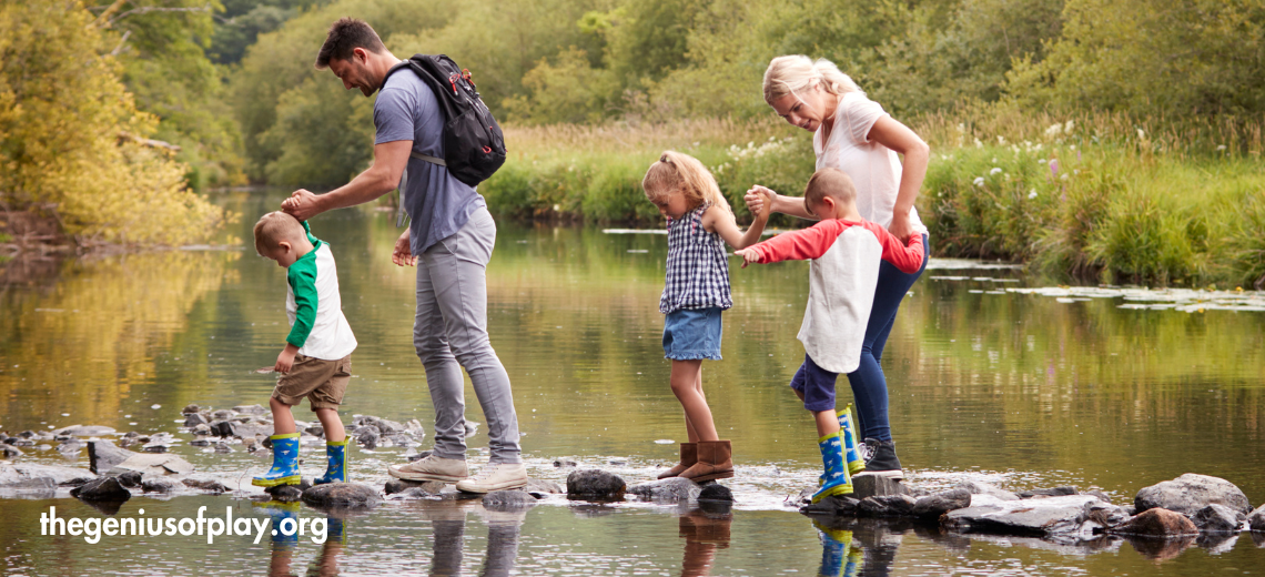 set of parents and two young children walking on rocks to cross over a river on a sunny afternoon